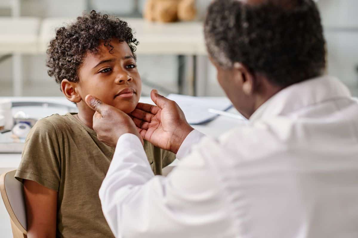 Pediatrics-Tonsil-Infection-exam Doctor in clinical setting feeling a child's throat area as part of a diagnosis